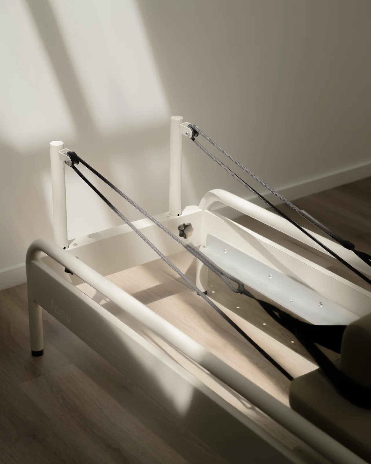 Window light raking across a cream fonv reformer's ropes and carriage.