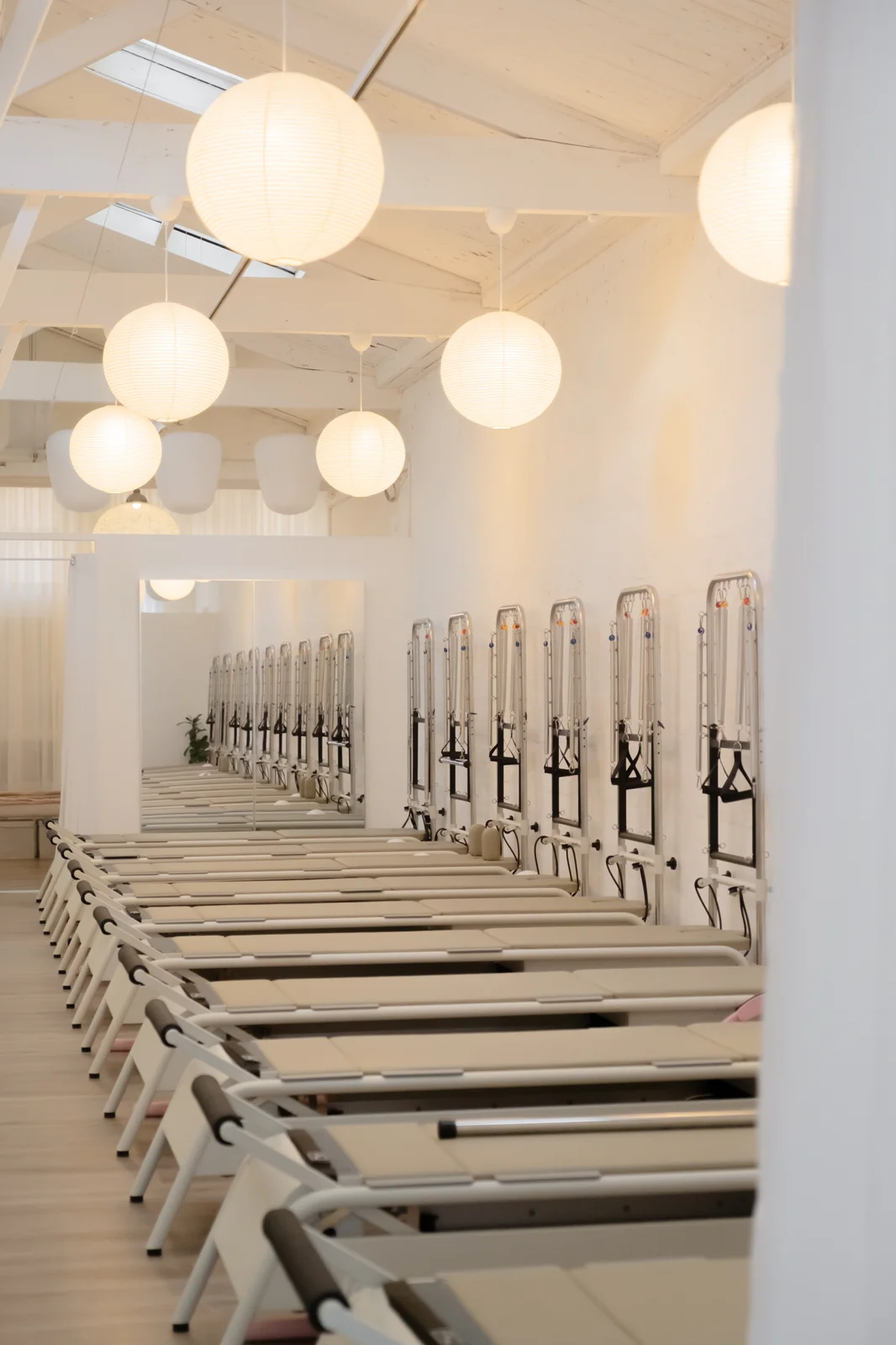 A long training hall of paired reformers and tower units beneath rows of glowing paper lanterns.