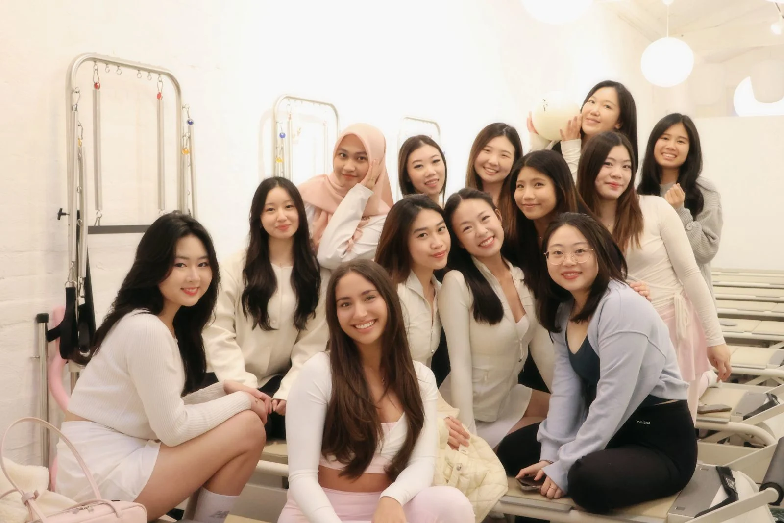 A smiling group of a dozen trainees gathered close among the reformers and towers of a bright white studio.
