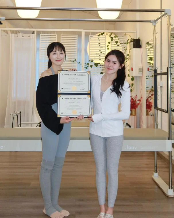 Annabel and her trainer holding her framed FONV certificates of completion in the training studio.