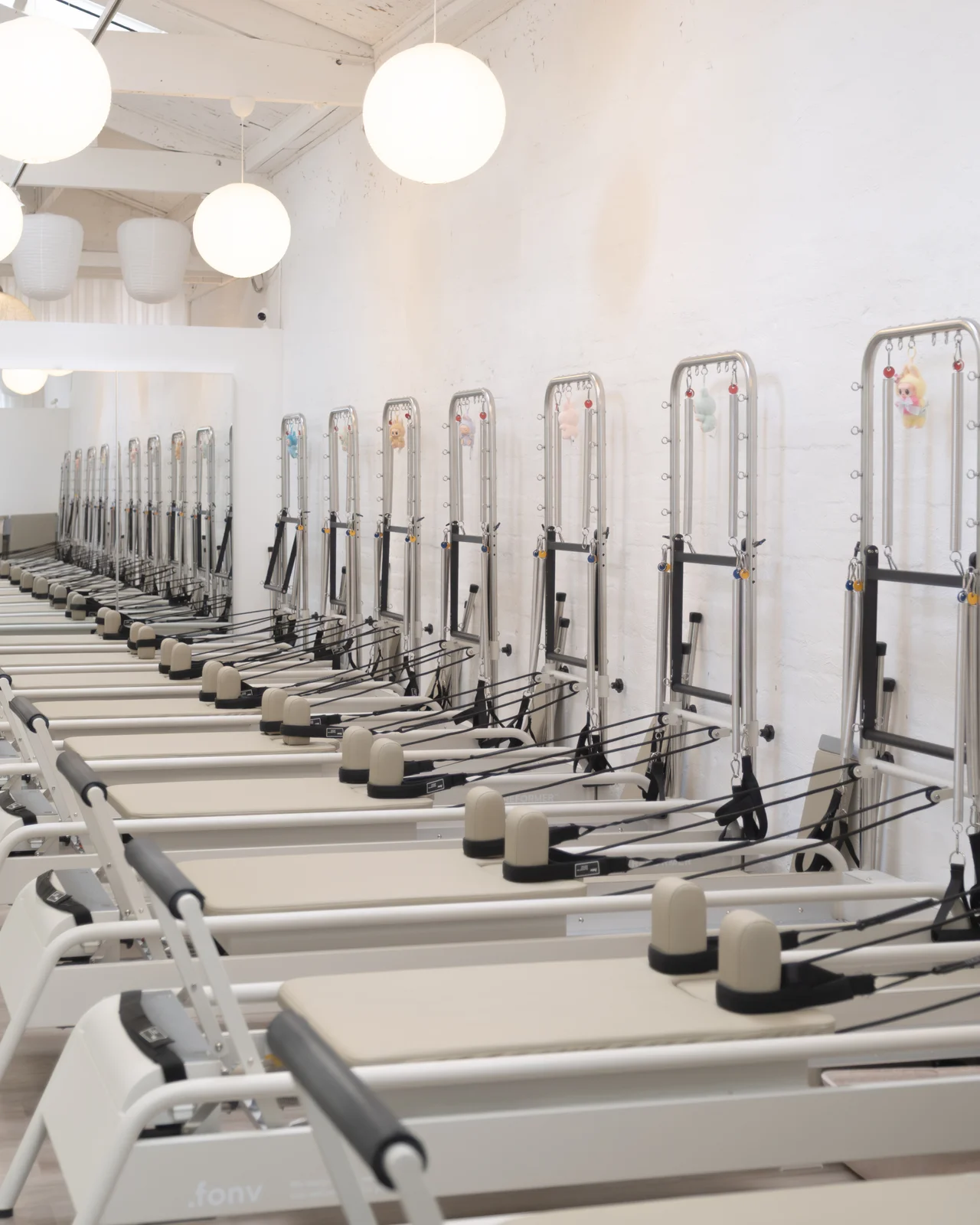Rows of cream reformers with tower frames under round paper lanterns in the white-washed CBD studio.